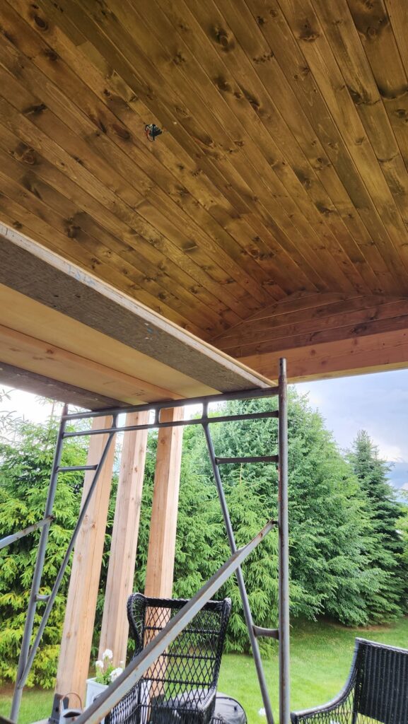 Stained tongue and groove wood ceiling on a covered porch under construction with scaffolding and wooden posts