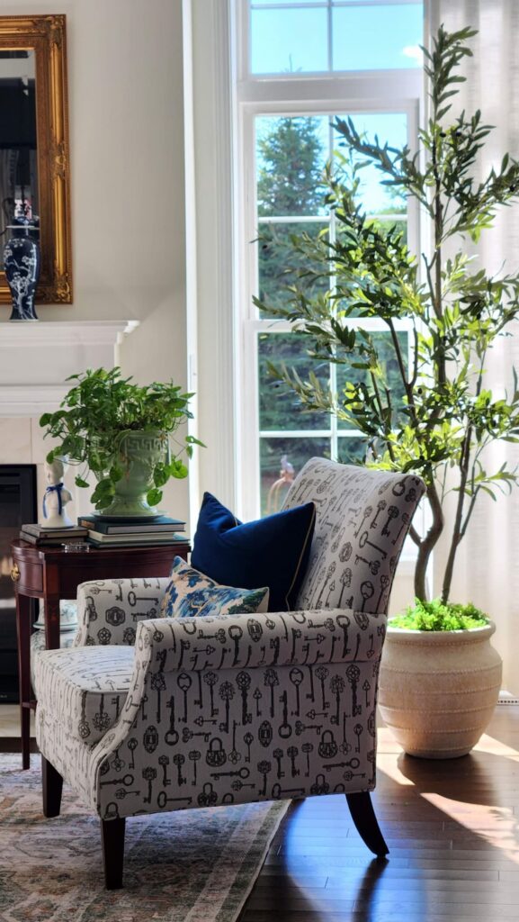 Bright living room corner with a tall faux olive tree, key-print accent chair, and navy blue pillows