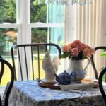 French country dining room with blue and white toile tablecloth, peach roses in an ironstone pitcher, white ceramic rooster, and antique bronze crystal chandelier — simple spring home decorating ideas