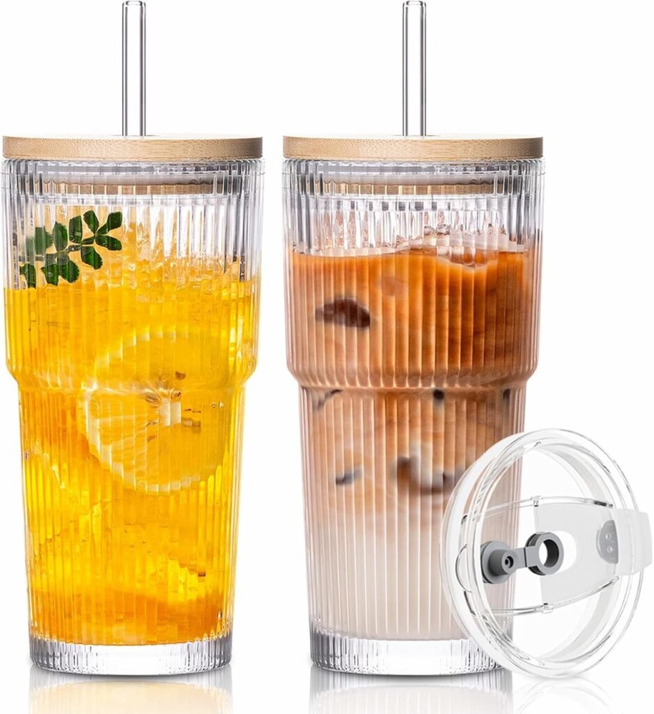 Two ribbed glass tumblers with bamboo lids and glass straws filled with iced drinks